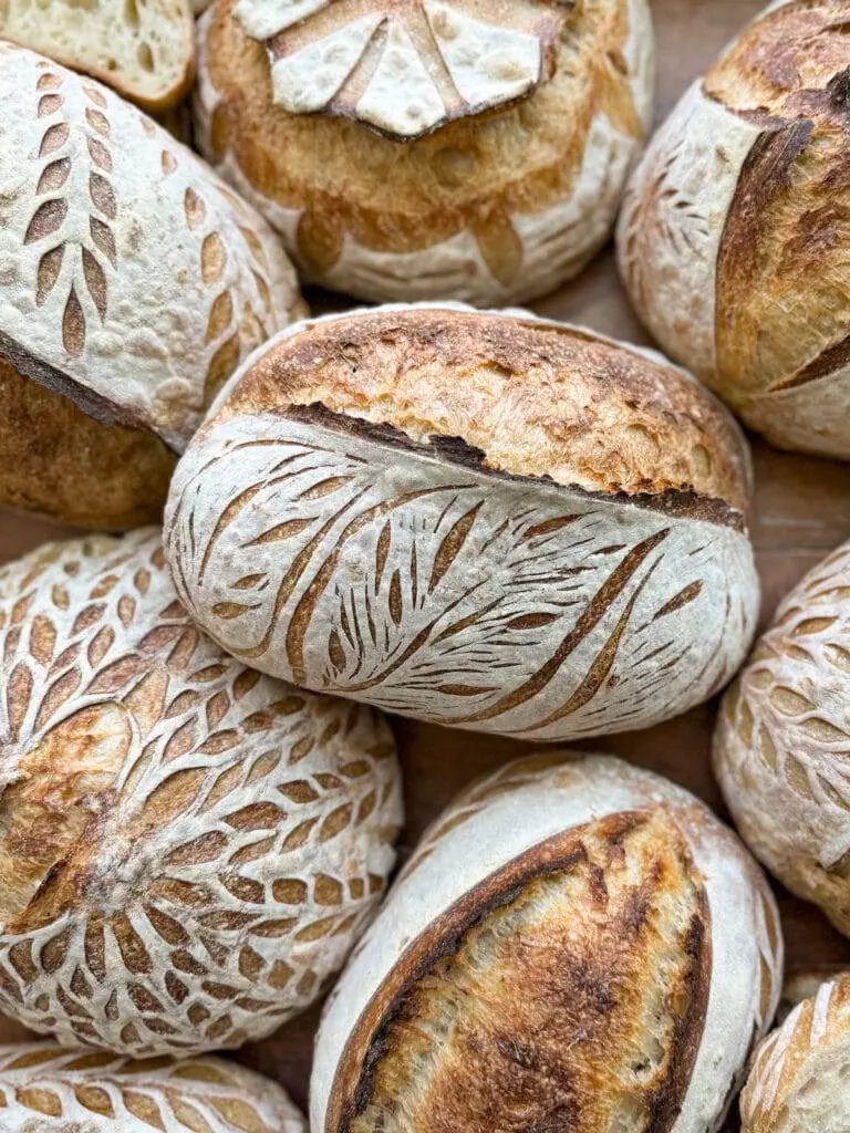 Several loaves of sourdough bread, with crusts scored with different designs.