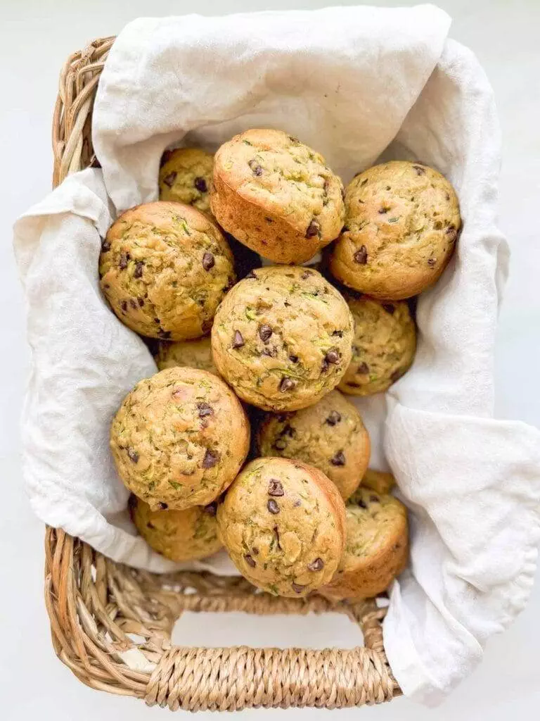 A linen lined basket full of zucchini muffins with chocolate chips.